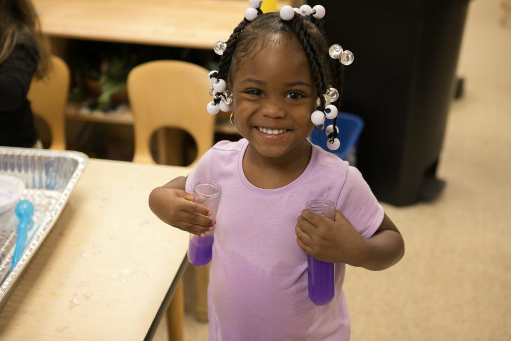 A preschool girl smiles while playing with two plastic containers of water