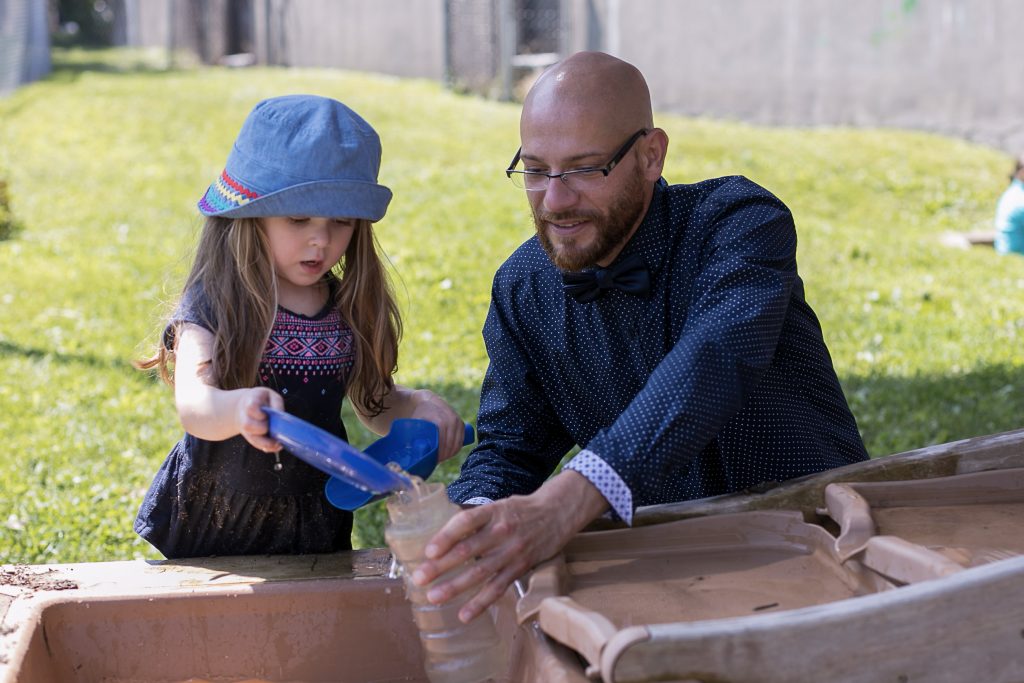 A teacher plays with a child at an outside water table