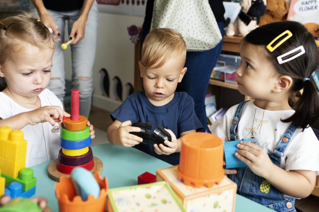 Three preschool children playing with blocks at a table.